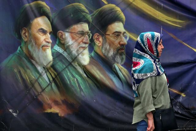 An Iranian woman walks past a billboard bearing the images of the late founder of the Islamic Revolution supreme leader Ayatollah Ruhollah Khomeini (L), the late Iranian supreme leader Ali Khamenei assassinated in February 2026, and his son, the current supreme leader Mojtaba Khamenei (R), erected along a street in Tehran on May 28, 2026. Iran's foreign ministry condemned on May 28, what it called violations by the United States after its strikes on the southern port city of Bandar Abbas and expressed solidarity with Oman after the US president threatened to "blow them up". (Photo by AFP) / 