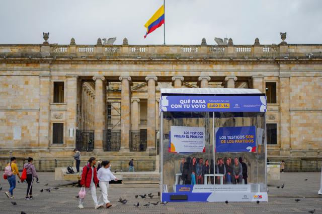 People walk at Bolivar Square next to posters on the upcoming presidential election in Bogota on May 28, 2026. Colombia will hold presidential elections on May 31, 2026. (Photo by Sergio ANGEL / AFP)