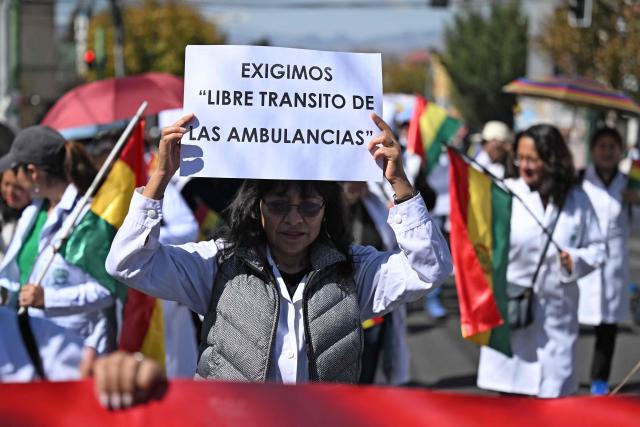 A healthcare worker holds a sign reading "We demand unimpeded access for ambulances" during a protest against roadblocks and access blockades to the city carried out by demonstrators opposing Bolivian President Rodrigo Paz, denouncing that shortages of food, medicines and oxygen are affecting patient care, in La Paz, Bolivia, on May 28, 2026. (Photo by Marvin RECINOS / AFP)
