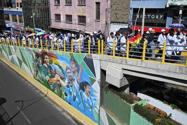 Doctors, nurses and other healthcare workers protest past a mural depicting Argentina's footballer Lionel Messi and Bolivia's footballer Marcelo Martins Moreno, against roadblocks and access blockades to the city carried out by demonstrators opposing Bolivian President Rodrigo Paz, denouncing that shortages of food, medicines and oxygen are affecting patient care, in La Paz, Bolivia, on May 28, 2026. (Photo by Marvin RECINOS / AFP)