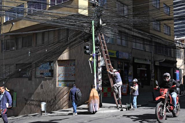Worker of the National Electricity Company (ENDE) handle cables on a central street in La Paz on May 28, 2026. The disorderly accumulation of overhead wiring on the city’s utility poles forms an urban web that poses a constant risk to pedestrians and drivers, while also generating significant visual pollution. (Photo by Aizar RALDES / AFP)