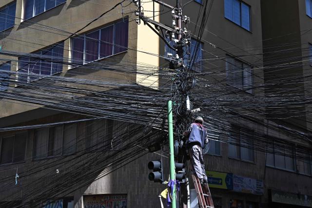 A worker of the National Electricity Company (ENDE) handles cables on a central street in La Paz on May 28, 2026. The disorderly accumulation of overhead wiring on the city’s utility poles forms an urban web that poses a constant risk to pedestrians and drivers, while also generating significant visual pollution. (Photo by Aizar RALDES / AFP)
