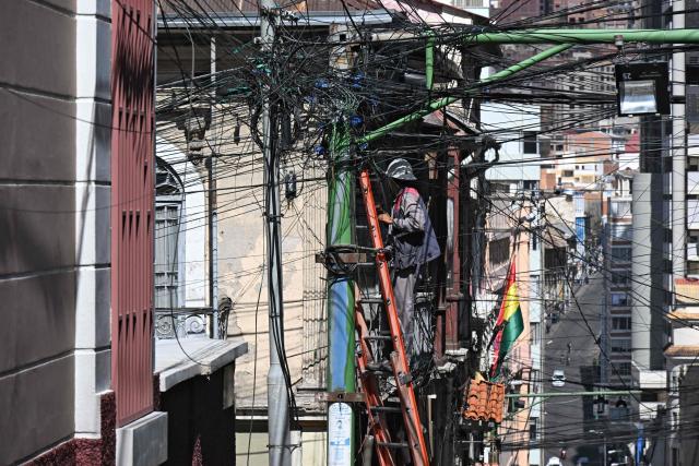 A worker of the National Electricity Company (ENDE) handles cables on a central street in La Paz on May 28, 2026. The disorderly accumulation of overhead wiring on the city’s utility poles forms an urban web that poses a constant risk to pedestrians and drivers, while also generating significant visual pollution. (Photo by Aizar RALDES / AFP)