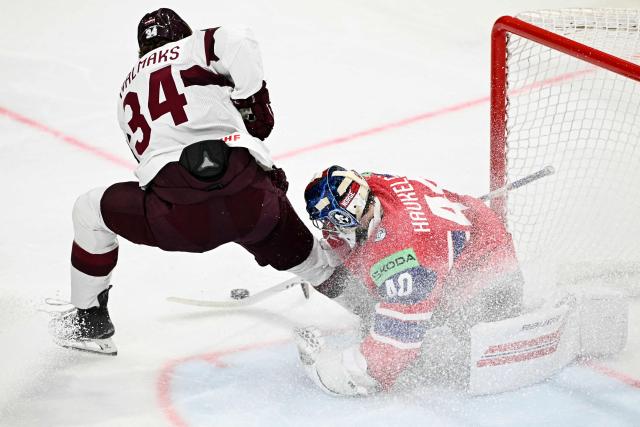 Latvia's forward #34 Eduards Tralmaks (L) and Norway's goalkeeper #40 Henrik Haukeland vie for the puck during the IIHF Ice Hockey Men's World Championship quarter-final match between Norway and Latvia in Fribourg, Switzerland on May 28, 2026. (Photo by Fabrice COFFRINI / AFP)