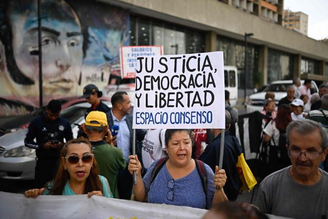 A woman holds a sing reading "Justice, Democracy and Freedom" during a protest demanding better living conditions and higher pensions on Venezuela’s National Older Adults Day, in Caracas, on May 29, 2026. (Photo by Federico PARRA / AFP)