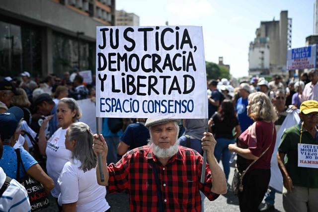 A man holds a sing reading "Justice, Democracy and Freedom" during a protest demanding better living conditions and higher pensions on Venezuela’s National Older Adults Day, in Caracas, on May 29, 2026. (Photo by Federico PARRA / AFP)