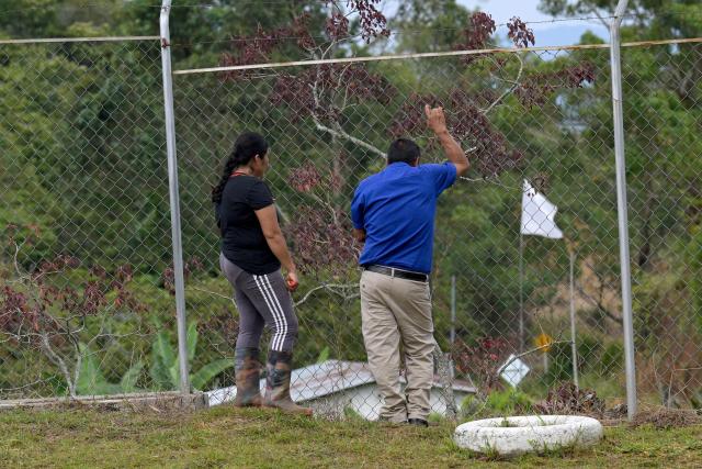 Colombian school teacher Flor Valencia (L) and social leader Jose Moran (R) look through a fence at a school near Suarez, Cauca department, Colombia on May 27, 2026. Surrounded by Andean mountains shrouded in clouds and tropical vegetation, Suarez is a rural village in the Cauca department located near a military base that is constantly under attack by dissident groups that broke away from the 2016 peace agreement with the now-defunct FARC guerrilla group. Locals will elect the successor to President Gustavo Petro on May 31, 2026, the first left-wing leader in the country's history who unsuccessfully attempted to negotiate peace with armed groups. (Photo by Joaquín SARMIENTO / AFP)