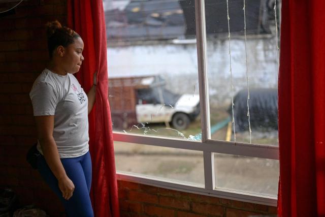 Colombian hotel administrator Tania Cervantes looks through a broken window at her hotel in Suarez, Cauca department, Colombia on May 27, 2026. Surrounded by Andean mountains shrouded in clouds and tropical vegetation, Suarez is a rural village in the Cauca department located near a military base that is constantly under attack by dissident groups that broke away from the 2016 peace agreement with the now-defunct FARC guerrilla group. Locals will elect the successor to President Gustavo Petro on May 31, 2026, the first left-wing leader in the country's history who unsuccessfully attempted to negotiate peace with armed groups. (Photo by Joaquín SARMIENTO / AFP)