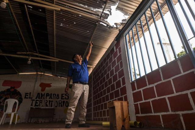Colombian social leader Jose Moran points to a hole in a roof caused by an explosion in Suarez, Cauca department, Colombia on May 27, 2026. Surrounded by Andean mountains shrouded in clouds and tropical vegetation, Suarez is a rural village in the Cauca department located near a military base that is constantly under attack by dissident groups that broke away from the 2016 peace agreement with the now-defunct FARC guerrilla group. Locals will elect the successor to President Gustavo Petro on May 31, 2026, the first left-wing leader in the country's history who unsuccessfully attempted to negotiate peace with armed groups. (Photo by Joaquín SARMIENTO / AFP)