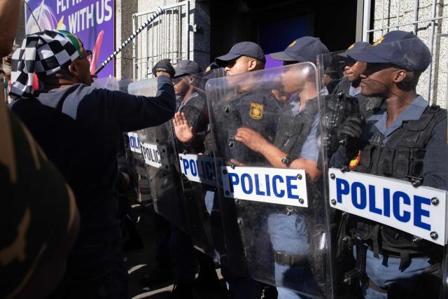 South African Police Service officers block access to a building used by drug dealers to a group of people, many carrying sticks and clubs, during a protest against illegal immigrants organised by March and March in Goodwood, a Cape Town suburb, on May 30, 2026. (Photo by RODGER BOSCH / AFP)