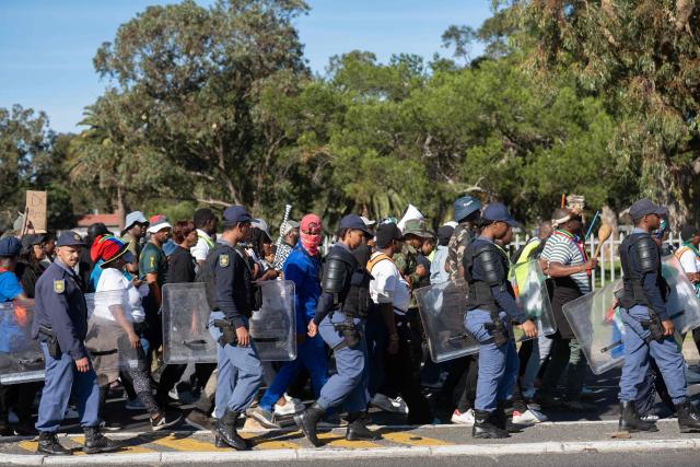 South African Police Service officers carrying riot shields monitor a group of people, many carrying sticks and clubs, as they take part in a protest against illegal immigrants organised by March and March in Goodwood, a Cape Town suburb, on May 30, 2026. (Photo by RODGER BOSCH / AFP)