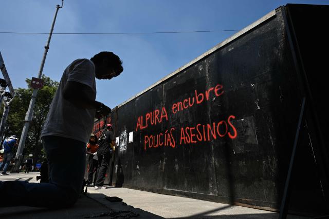 A man prays with a rosary in front of a metal fence—painted with graffiti by members of collectives searching for missing persons—where they are affixing missing-person flyers for their relatives while participating in a day of protest outside Mexico City Stadium, which will host the opening ceremony of the upcoming FIFA World Cup, in Mexico City on May 30, 2026. (Photo by Yuri CORTEZ / AFP)