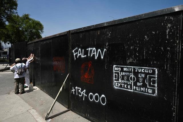 Members of collectives searching for missing persons paint graffiti on a metal fence while participating in a day of protest in front of Mexico City Stadium, which will host the opening ceremony of the upcoming FIFA World Cup, in Mexico City on May 30, 2026. (Photo by Yuri CORTEZ / AFP)