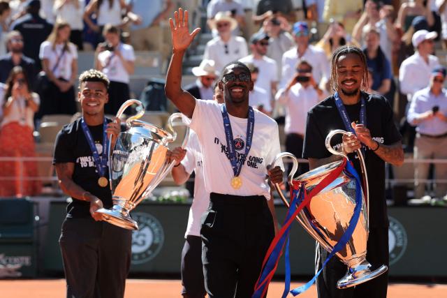 (From L) Paris Saint-Germain's French midfielder #14 Desire Doue, Paris Saint-Germain's French forward #10 Ousmane Dembele and Paris Saint-Germain's French forward #29 Bradley Barcola hold the two UEFA Champions League's trophies on day 9 of the French Open tennis tournament on Court Philippe-Chatrier at the Roland-Garros Complex in Paris on June 1, 2026. Paris Saint-Germain (PSG) claimed back-to-back Champions League triumphs with a 4-3 shoot-out win over Arsenal following a 1-1 draw after extra time at the Puskas Arena in Budapest on May 30, 2026. (Photo by Thomas SAMSON / AFP)