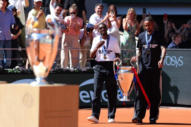 Paris Saint-Germain's French forward #10 Ousmane Dembele (L) and Paris Saint-Germain's French forward #29 Bradley Barcola bring the UEFA Champions League's trophy on day 9 of the French Open tennis tournament on Court Philippe-Chatrier at the Roland-Garros Complex in Paris on June 1, 2026. Paris Saint-Germain (PSG) claimed back-to-back Champions League triumphs with a 4-3 shoot-out win over Arsenal following a 1-1 draw after extra time at the Puskas Arena in Budapest on May 30, 2026. (Photo by Thomas SAMSON / AFP)