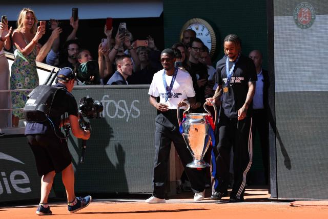 Paris Saint-Germain's French forward #10 Ousmane Dembele (L) and Paris Saint-Germain's French forward #29 Bradley Barcola bring the UEFA Champions League's trophy on day 9 of the French Open tennis tournament on Court Philippe-Chatrier at the Roland-Garros Complex in Paris on June 1, 2026. Paris Saint-Germain (PSG) claimed back-to-back Champions League triumphs with a 4-3 shoot-out win over Arsenal following a 1-1 draw after extra time at the Puskas Arena in Budapest on May 30, 2026. (Photo by Thomas SAMSON / AFP)