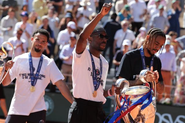(Frm L) Paris Saint-Germain's French midfielder #33 Warren Zaire-Emery, Paris Saint-Germain's French forward #10 Ousmane Dembele and Paris Saint-Germain's French forward #29 Bradley Barcola bring the two UEFA Champions League's trophies on day 9 of the French Open tennis tournament on Court Philippe-Chatrier at the Roland-Garros Complex in Paris on June 1, 2026. Paris Saint-Germain (PSG) claimed back-to-back Champions League triumphs with a 4-3 shoot-out win over Arsenal following a 1-1 draw after extra time at the Puskas Arena in Budapest on May 30, 2026. (Photo by Thomas SAMSON / AFP)