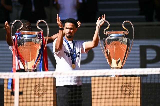 Paris Saint-Germain's French midfielder #33 Warren Zaire-Emery waves at spectators next to the two UEFA Champions League's trophies on day 9 of the French Open tennis tournament on Court Philippe-Chatrier at the Roland-Garros Complex in Paris on June 1, 2026. Paris Saint-Germain (PSG) claimed back-to-back Champions League triumphs with a 4-3 shoot-out win over Arsenal following a 1-1 draw after extra time at the Puskas Arena in Budapest on May 30, 2026. (Photo by JULIEN DE ROSA / AFP)