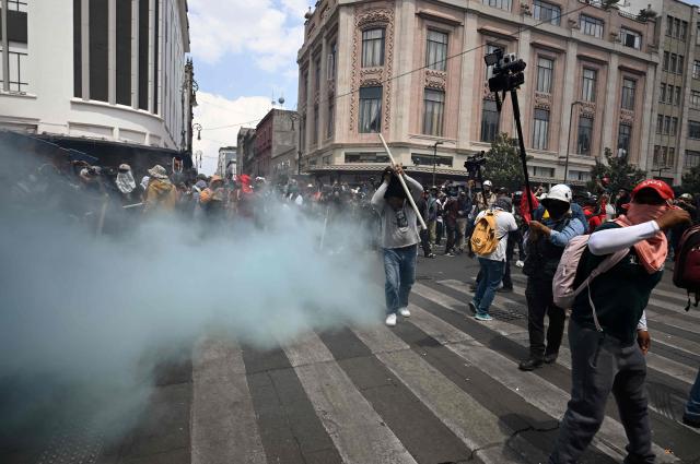 Teachers stand near a barricade blocking access to the Zocalo as blue smoke from a fire extinguisher discharged by police rises from the other side during a demonstration ahead of the FIFA World Cup 2026, in Mexico City on June 1, 2026. (Photo by Alfredo ESTRELLA / AFP)