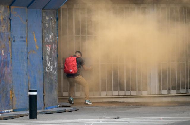 A teacher stands near a barricade blocking access to the Zocalo as orange smoke from a fire extinguisher discharged by police rises from the other side during a demonstration ahead of the FIFA World Cup 2026, in Mexico City on June 1, 2026. (Photo by Alfredo ESTRELLA / AFP)
