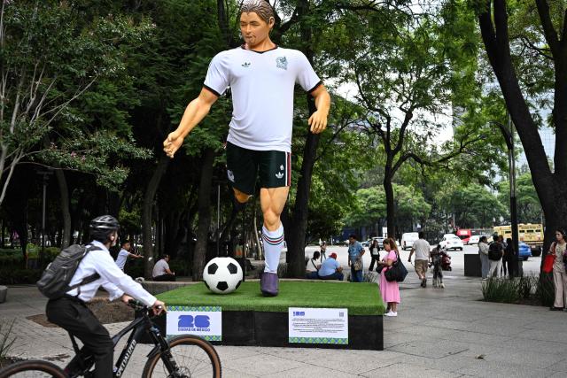 People walk past a giant sculpture depicting a Mexico's football player, as part of the urban exhibition "Gigantes del Futbol" (Giants of Soccer) by Mexican artisans from the Zion Art Studio workshop, ahead of the FIFA 2026 World Cup in Mexico City on June 1, 2026. (Photo by Yuri CORTEZ / AFP)