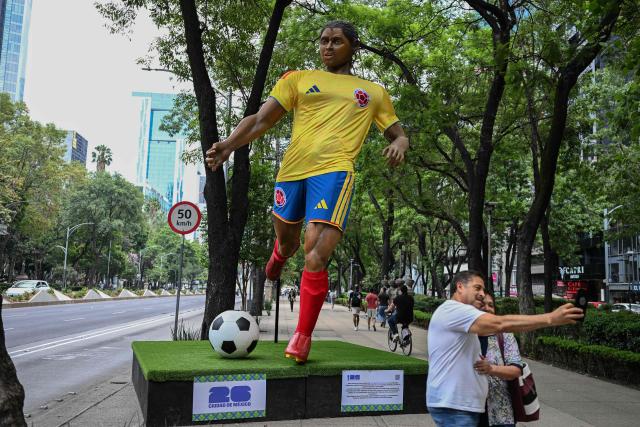 A couple take a selfie nexto to a giant sculpture depicting a Colombia's football player, as part of the urban exhibition "Gigantes del Futbol" (Giants of Soccer) by Mexican artisans from the Zion Art Studio workshop, ahead of the FIFA 2026 World Cup in Mexico City on June 1, 2026. (Photo by Yuri CORTEZ / AFP)