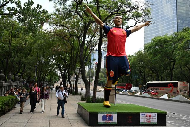 People walk past a giant sculpture depicting a Spain's football player, as part of the urban exhibition "Gigantes del Futbol" (Giants of Soccer) by Mexican artisans from the Zion Art Studio workshop, ahead of the FIFA 2026 World Cup in Mexico City on June 1, 2026. (Photo by Yuri CORTEZ / AFP)