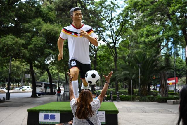 A woman gesture in front of a giant sculpture depicting a Germany's football player, as part of the urban exhibition "Gigantes del Futbol" (Giants of Soccer) by Mexican artisans from the Zion Art Studio workshop, ahead of the FIFA 2026 World Cup in Mexico City on June 1, 2026. (Photo by Yuri CORTEZ / AFP)