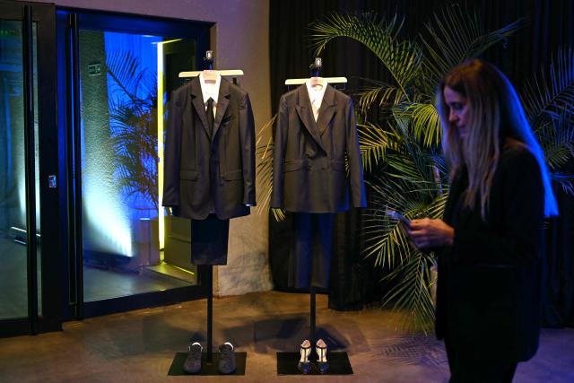 A woman checks her phone in front of the official suits for Uruguay's national football team designed by Uruguayan-US fashion designer Gabriela Hearst for the 2026 FIFA World Cup, at the Centenario Stadium in Montevideo on June 2, 2026. The outfits, designed by Hearst, were made from Uruguayan merino wool. (Photo by Eitan ABRAMOVICH / AFP)