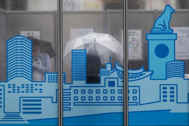 People smoke under their umbrellas in a smoking booth as severe tropical storm Jangmi passes over Tokyo on June 3, 2026. (Photo by ANDREW CABALLERO-REYNOLDS / AFP)
