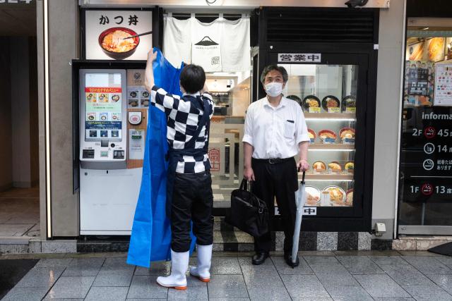 A man waits under cover as an employee puts up a rain cover as severe tropical storm Jangmi passes over Tokyo on June 3, 2026. (Photo by ANDREW CABALLERO-REYNOLDS / AFP)