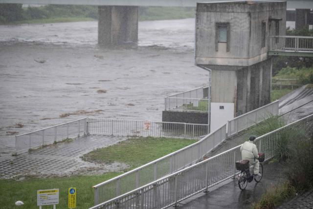 A?man cycles past the Tama river amid heavy rain brought by severe tropical storm Jangmi in Tokyo on June 3, 2026. (Photo by Yuichi YAMAZAKI / AFP)