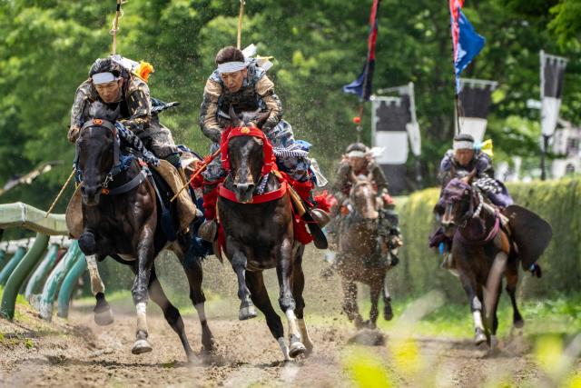 Horsemen clad in samurai armor compete in the Kachu Keiba race during the Soma Nomaoi festival at Hibarigahara field in Minamisoma, Fukushima prefecture on May 24, 2026. The Soma Nomaoi began as a way to train mounted warriors and it still looks the same a millennium later, with riders dressed in samurai armour battling it out in horseback events. (Photo by Yuichi YAMAZAKI / AFP) / To go with 'Japan-Climate-Festival-Tradition' Focus by Andrew MCKIRDY