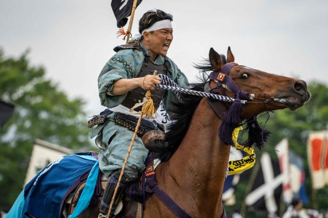 A horseman clad in samurai armor reacts as he catches a flag in the Shinki-soudatsusen sacred flag competition during the Soma Nomaoi festival at Hibarigahara field in Minamisoma, Fukushima prefecture on May 24, 2026. The Soma Nomaoi began as a way to train mounted warriors and it still looks the same a millennium later, with riders dressed in samurai armour battling it out in horseback events. (Photo by Yuichi YAMAZAKI / AFP) / To go with 'Japan-Climate-Festival-Tradition' Focus by Andrew MCKIRDY