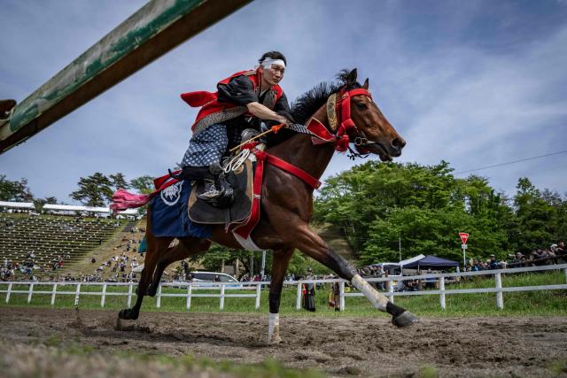 In this picture taken on May 23, 2026, a horseman clad in samurai armor competes in the Yoinori Keiba race during the Soma Nomaoi festival at Hibarigahara field in Minamisoma, Fukushima prefecture. The Soma Nomaoi began as a way to train mounted warriors and it still looks the same a millennium later, with riders dressed in samurai armour battling it out in horseback events. (Photo by Yuichi YAMAZAKI / AFP) / To go with 'Japan-Climate-Festival-Tradition' Focus by Andrew MCKIRDY