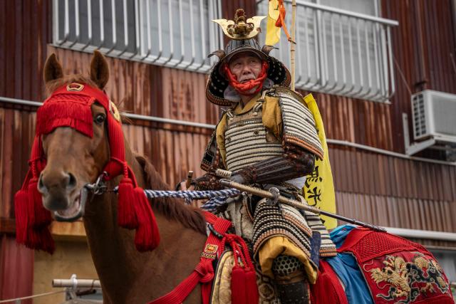 This picture taken on May 24, 2026 shows Mitsukiyo Monma leaving his house for a parade during the Soma Nomaoi festival in Minamisoma, Fukushima prefecture. The Soma Nomaoi began as a way to train mounted warriors and it still looks the same a millennium later, with riders dressed in samurai armour battling it out in horseback events. (Photo by Yuichi YAMAZAKI / AFP)