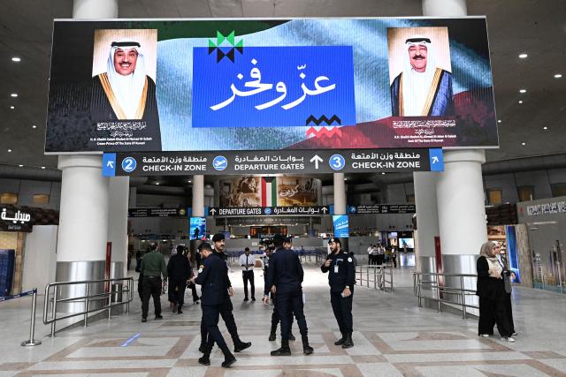 TOPSHOT - (FILES) Kuwaiti security officers stand beneath a screen displaying portraits of the Emir of Kuwait Sheikh Meshal al-Ahmad al-Jaber al-Sabah (R) and the Kuwaiti crown prince Sheikh Sabah al-Khaled al-Hamad al-Sabah, alongside the words "Pride and Glory", at Kuwait International Airport in Kuwait City on June 1, 2026, as the airport resumes operations following a phased reopening plan. Iran carried out a drone strike on a passenger terminal at Kuwait International Airport, wounding several people and forcing air traffic to be suspended, Kuwaiti officials said on June 3. (Photo by YASSER AL-ZAYYAT / AFP)