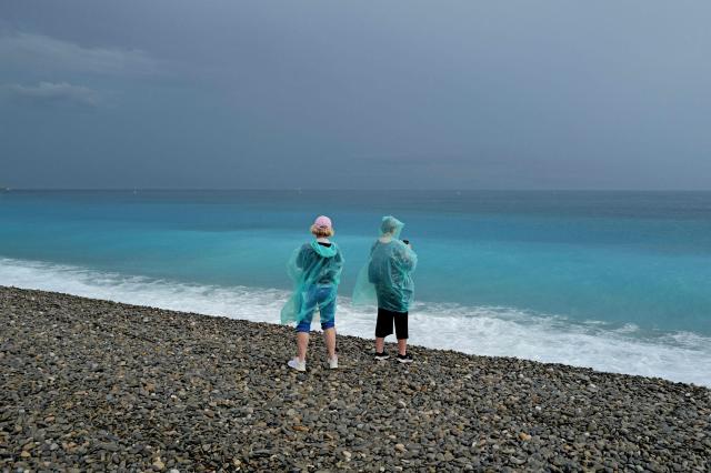 Two women walk on a shingle beach as they take images of The Mediterranean Sea along the "Promenade des anglais" in the French riviera city of Nice on June 2, 2026. (Photo by Valery HACHE / AFP)