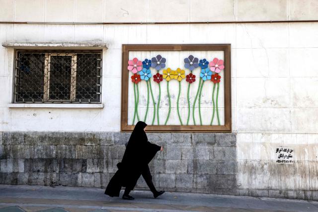 TOPSHOT - An Iranian woman walks past a piece of street art in Tehran on June 3, 2026. The military adviser to Iran's supreme leader on June 3, warned of more missile and drone strikes should the United States renew its attacks on Iran. The warning followed US strikes on an Iranian tanker and on Iran's Qeshm island, sparking retaliatory attacks on Kuwait and Bahrain. (Photo by ATTA KENARE / AFP) / 