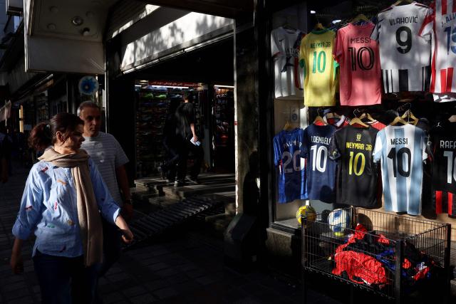 Iranians walk past a shop displaying football jerseys for sale in Tehran on May 8, 2026. Iran's national team, also known as TeamMelli, open their 2026 World Cup campaign, co-hosted by the United States, Mexico and Canada, against New Zealand in Los Angeles on June 15 before lining up against Belgium and Egypt in Group G. Iran has been at war with the United States and Israel since February 28, though a fragile ceasefire has been in place since April 8. Tehran and Washington have had no diplomatic relations since 1980 following the hostage crisis at the US embassy, which came after the Islamic revolution that toppled the US-backed shah. (Photo by AFP)