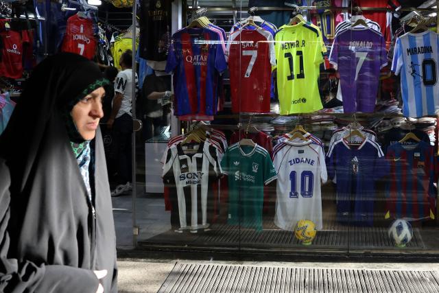 An Iranian woman walks past a shop displaying football jerseys for sale in Tehran on May 8, 2026. Iran's national team, also known as TeamMelli, open their 2026 World Cup campaign, co-hosted by the United States, Mexico and Canada, against New Zealand in Los Angeles on June 15 before lining up against Belgium and Egypt in Group G. Iran has been at war with the United States and Israel since February 28, though a fragile ceasefire has been in place since April 8. Tehran and Washington have had no diplomatic relations since 1980 following the hostage crisis at the US embassy, which came after the Islamic revolution that toppled the US-backed shah. (Photo by AFP)
