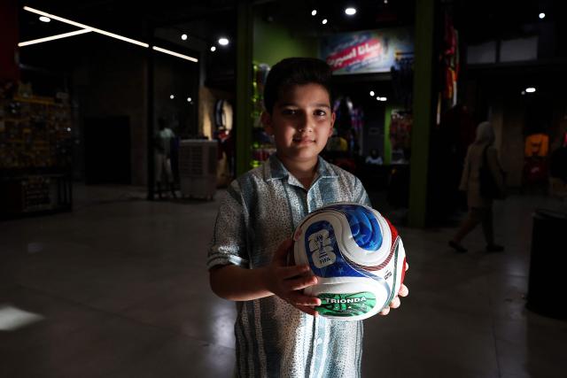 An Iranian boy holds a replica of the World Cup trophy displayed inside a shop in Tehran on May 8, 2026. Iran's national team, also known as TeamMelli, open their 2026 World Cup campaign, co-hosted by the United States, Mexico and Canada, against New Zealand in Los Angeles on June 15 before lining up against Belgium and Egypt in Group G. Iran has been at war with the United States and Israel since February 28, though a fragile ceasefire has been in place since April 8. Tehran and Washington have had no diplomatic relations since 1980 following the hostage crisis at the US embassy, which came after the Islamic revolution that toppled the US-backed shah. (Photo by AFP)