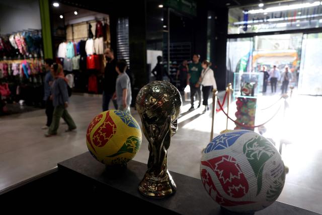 Iranians walk past a replica of the World Cup trophy in a sporting goods retailer in Tehran on May 8, 2026. Iran's national team, also known as TeamMelli, open their 2026 World Cup campaign, co-hosted by the United States, Mexico and Canada, against New Zealand in Los Angeles on June 15 before lining up against Belgium and Egypt in Group G. Iran has been at war with the United States and Israel since February 28, though a fragile ceasefire has been in place since April 8. Tehran and Washington have had no diplomatic relations since 1980 following the hostage crisis at the US embassy, which came after the Islamic revolution that toppled the US-backed shah. (Photo by AFP)