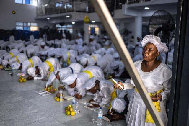A worshipper kneels in prayer as others pray beside thanksgiving items during a service at the Celestial Church of Christ International Headquarters in the Ketu neighbourhood of Lagos, on June 3, 2026. (Photo by OLYMPIA DE MAISMONT / AFP)