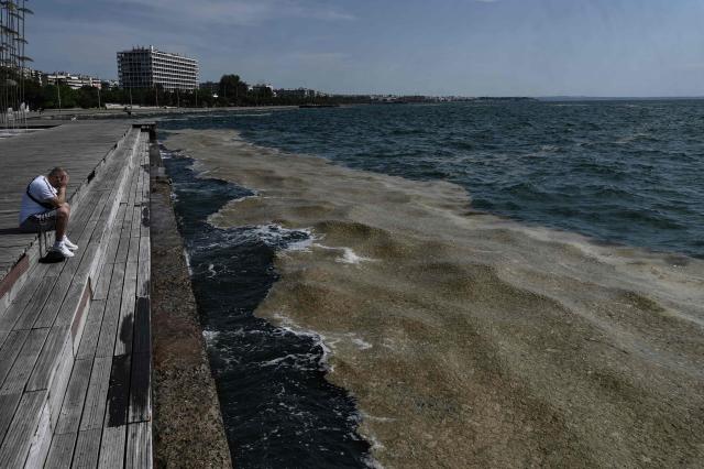 An onlooker sits on the seafront as phytoplankton covers an area of waterfront in Thessaloniki on June 3, 2026. Phytoplankton occurs in the area of the seafront of the Municipality of Thessaloniki due to the deterioration of the natural phenomenon of red tide in the Thermaikos Gulf. The phenomenon common in summer when high temperatures prevail together with southern winds. (Photo by Sakis Mitrolidis / AFP)