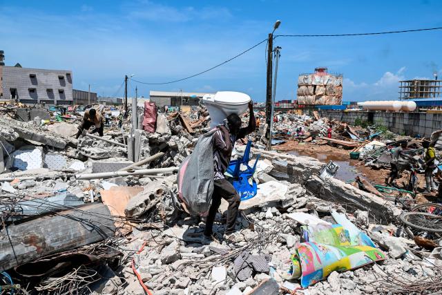 A young man walks with a toilet over rubble after the destruction of the precarious Zimbabwe neighbourhood during an eviction operation in the Port-Bouet neighbourhood in Abidjan on June 3, 2026. (Photo by Sia KAMBOU / AFP)
