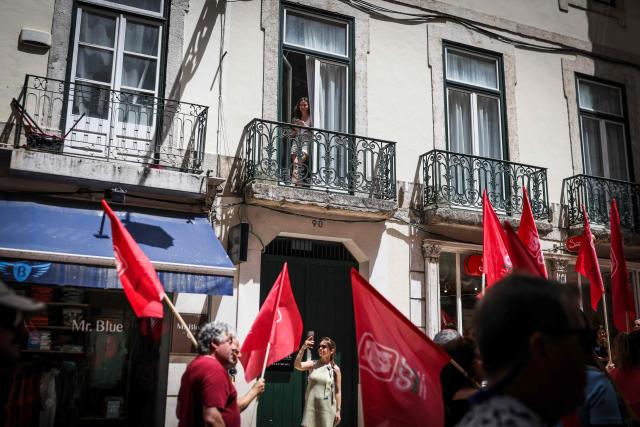 A woman peeps from a balcony as people take part in a demonstration in Lisbon on July 3, 2026, called by the main unions due to a 24-hour general strike over proposed labour reforms. The stoppage hit transport companies as well as waste collection, hospitals and schools, according to the General Confederation of Portuguese Workers (CGTP). (Photo by PATRICIA DE MELO MOREIRA / AFP)