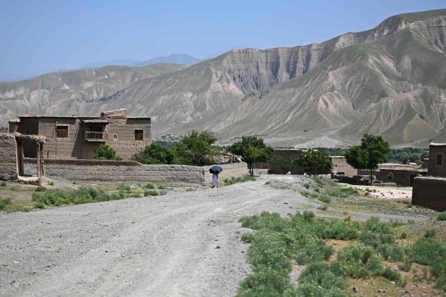 This photograph taken on May 18, 2026 shows an Afghan man carrying an umbrella as he walks along a street in the Char Bagh area of Doshi district, Baghlan province. Under the shade of recently planted poplars in northeastern Afghanistan, village leader Ghulam Ali Poya is proud to see residents rediscover the value of trees after years of wartime deforestation from the 1979 Soviet invasion until the fall of the first Taliban government in the early 2000s. Efforts are now underway to revive the landscape in communities across Afghanistan. (Photo by Wakil KOHSAR / AFP)