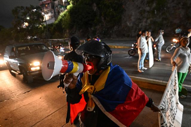 A demonstrator wrapped in a Venezuelan flag takes part in a demonstration to demand the freedom of political prisoners during a transfer outside El Helicoide prison in Caracas on June 3, 2026. (Photo by Juan BARRETO / AFP)
