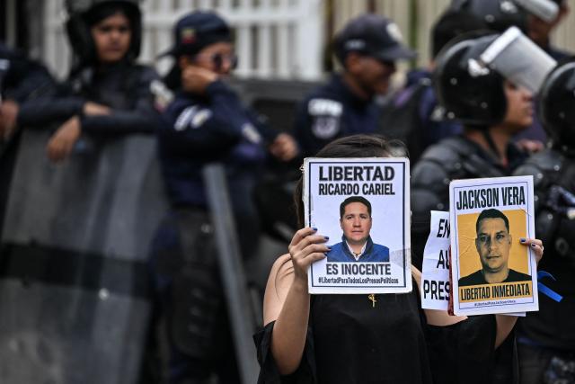 A woman shows signs demanding the freedom of political prisoners as Venezuela's Bolivarian National Police guard a prisoners' transfer outside El Helicoide prison in Caracas on June 3, 2026. (Photo by Juan BARRETO / AFP)